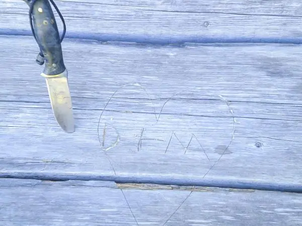 Messer liegt neben einer in Holz eingeritzten Herzform mit Initialen