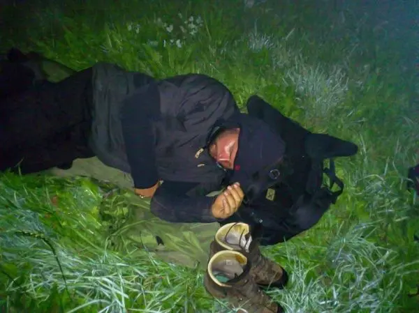 Person liegt auf einer Wiese, umgeben von Gras und Ausrüstung