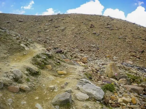 Schmaler Pfad führt über steinigen Hang mit großen Felsen und Grasbewuchs