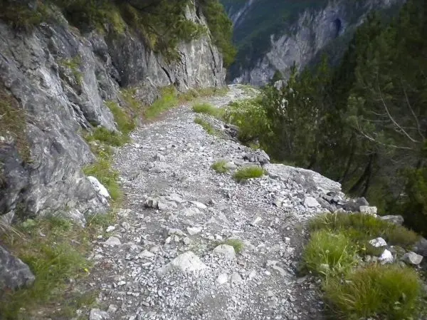 Schmaler, steiniger Pfad entlang einer Felswand mit grünem Bewuchs