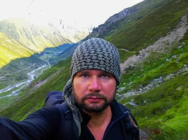 Selbstporträt in bergiger Landschaft mit Rucksack und Kopfbedeckung