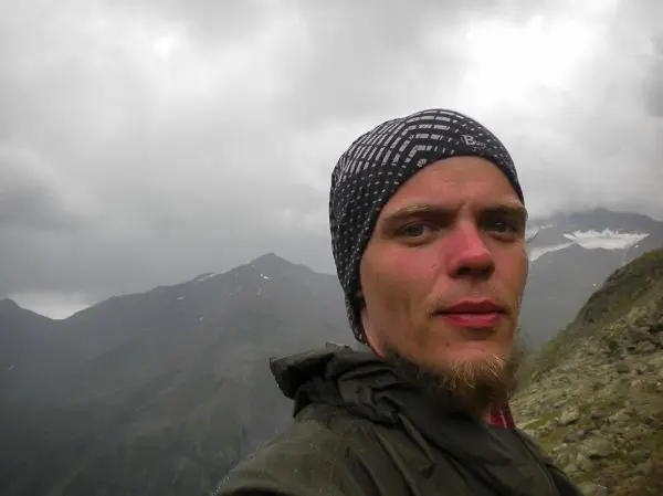 Selbstporträt vor einer bergigen Landschaft mit bewölktem Himmel