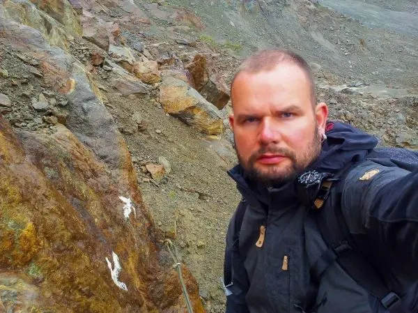 Selbstporträt vor felsigem Gelände mit sichtbaren Steinen und Erde