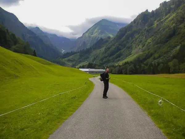 Wanderer auf einem Weg zwischen grünen Wiesen und Bergen