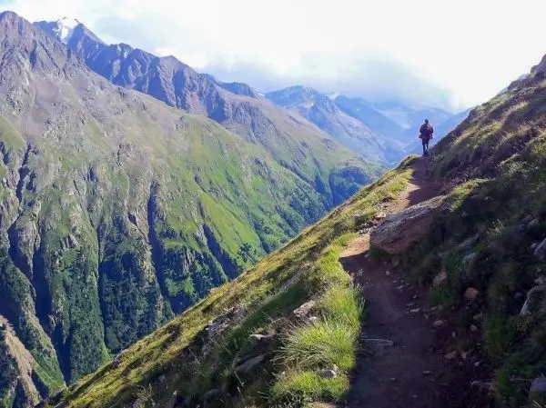 Wanderer auf schmalem Pfad entlang steiler Bergflanke mit grüner Vegetation