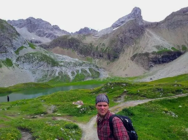 Wanderer mit Rucksack steht am Wegesrand in bergiger Landschaft mit See