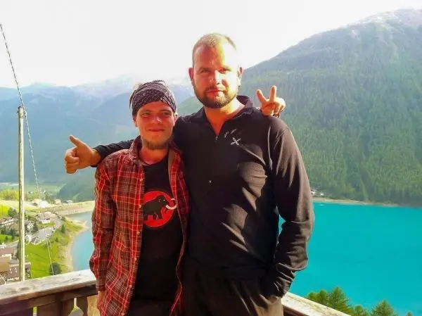 Zwei Männer stehen auf einem Balkon mit Blick auf einen See und Berge