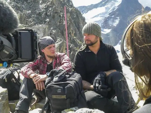 Zwei Personen sitzen auf einem Felsen, Rucksäcke und Kameraequipment sichtbar
