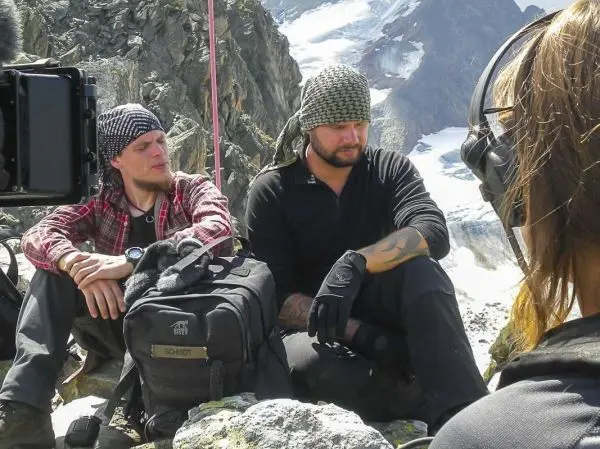 Zwei Personen sitzen auf Felsen, eine Kamera ist auf sie gerichtet