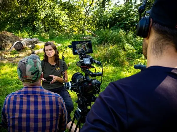 Kamera filmt Interview in der Natur mit zwei Personen und Holzstämmen im Hintergrund