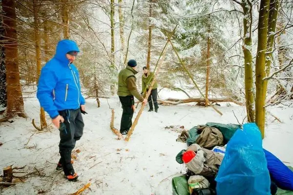 Drei Personen im Schnee, eine baut eine Struktur aus Holz