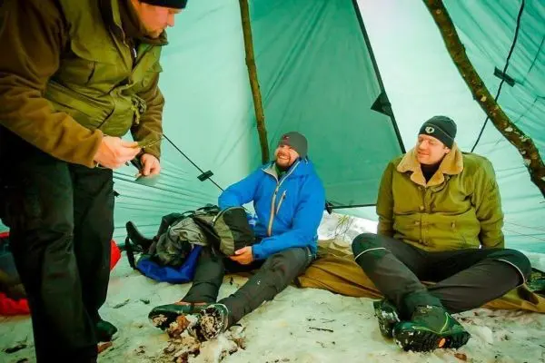 Drei Personen sitzen unter einem Zelt auf Schnee