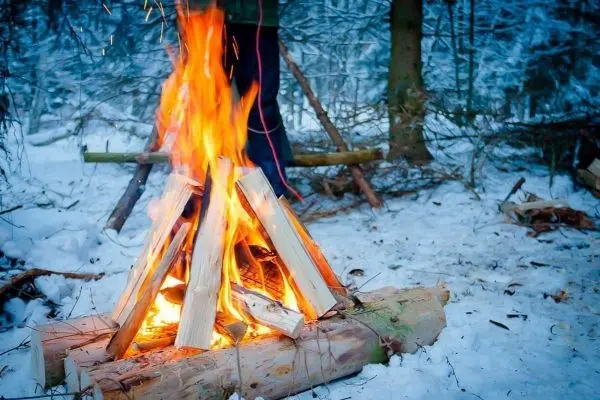 Feuer auf Holzscheiten im Schnee, Person im Hintergrund