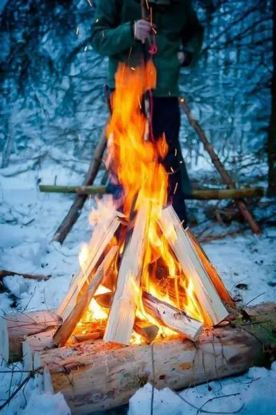 Feuerstelle mit brennendem Holz in verschneiter Umgebung