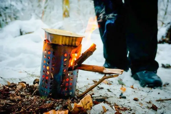 Feuerstelle mit Flammen und rauchendem Behälter im Schnee