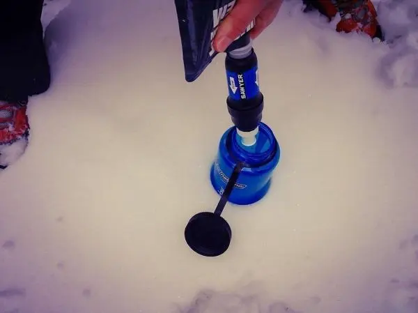 Hand hält Wasserfilter über blauen Behälter im Schnee