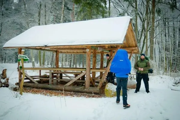 Holzhütte im Schnee mit drei Personen in der Nähe
