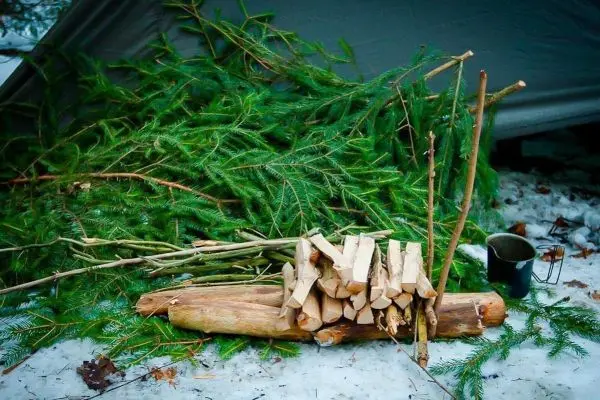 Holzstapel auf Schnee mit grünen Zweigen und einer Tasse