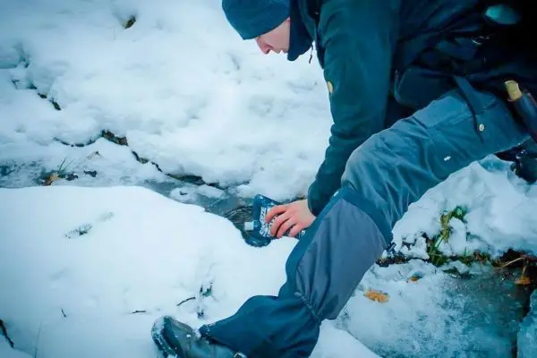 Person beugt sich über Schnee und Eis, hält ein Gerät in der Hand