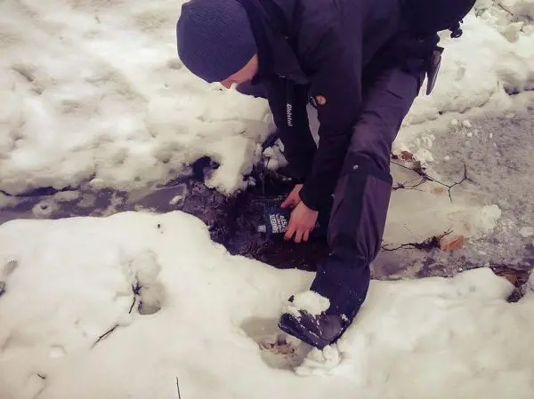 Person greift nach einem Gegenstand im Schnee und Wasser