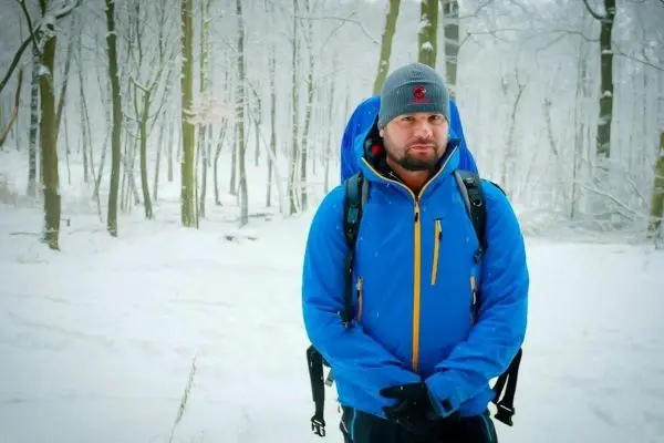 Person in blauer Jacke steht im verschneiten Wald