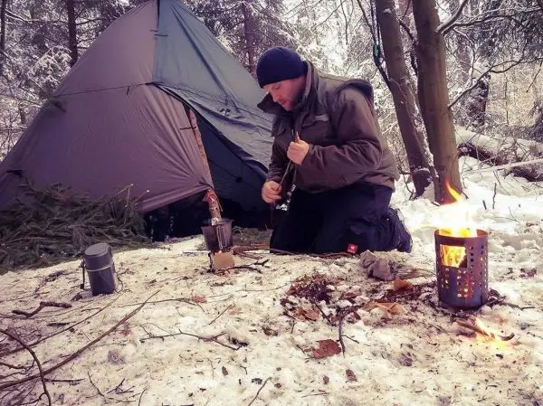 Person kniet im Schnee neben einem Zelt und bereitet Feuer vor