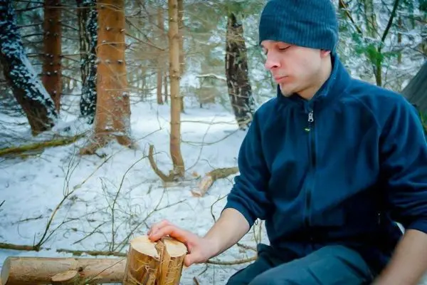 Person sitzt im Schnee und hält einen Holzscheit