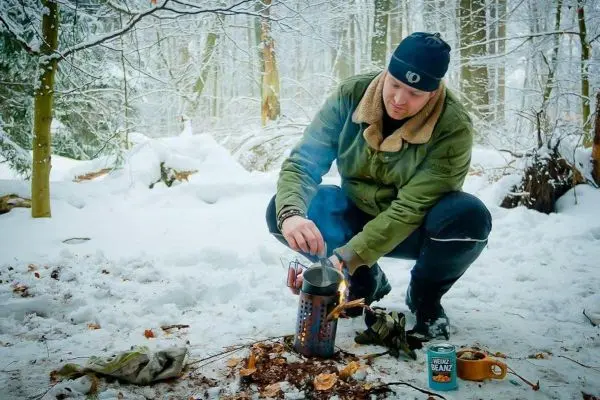 Person sitzt im Schnee und zündet einen Kocher an