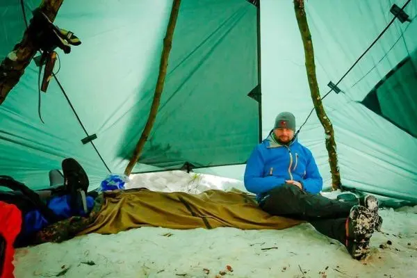 Person sitzt in einem Zelt auf Schnee, trägt blaue Jacke
