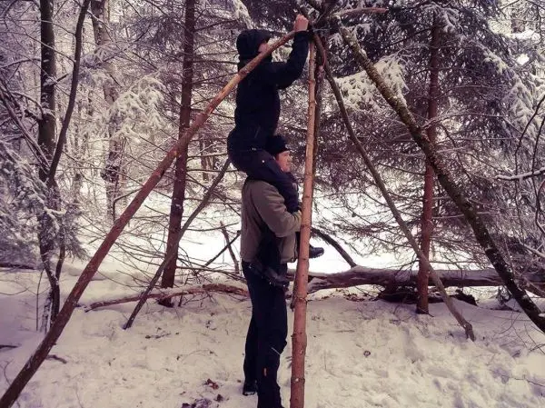 Person steht auf einer anderen Person und baut eine Struktur aus Ästen im Schnee