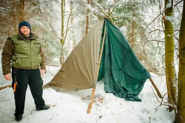 Person steht neben einem Zelt im Schneewald