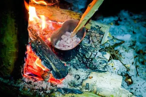 Topf mit Speisen über offenem Feuer auf Holzscheiten