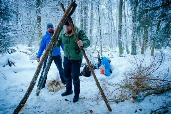 Zwei Personen im Schnee bauen eine Struktur aus Ästen