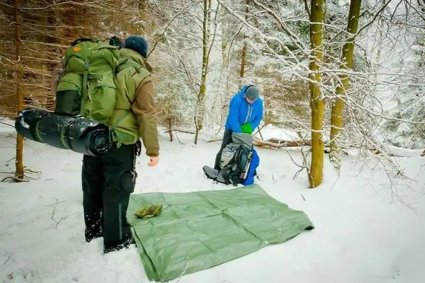 Zwei Personen im Schnee, eine bereitet eine grüne Plane vor