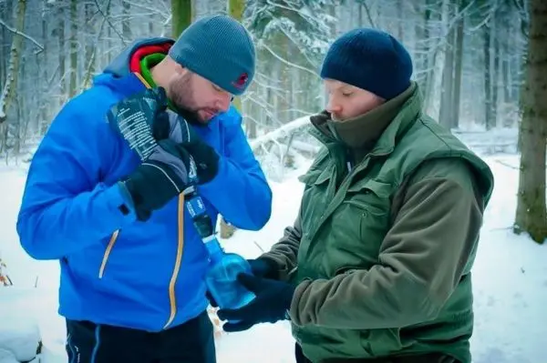Zwei Personen im Schnee, eine hält eine Flasche, die andere schaut zu