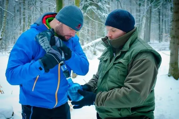Zwei Personen im Schnee, eine hält eine Wasserflasche