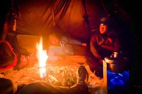 Zwei Personen sitzen in einem Zelt neben einem Feuer