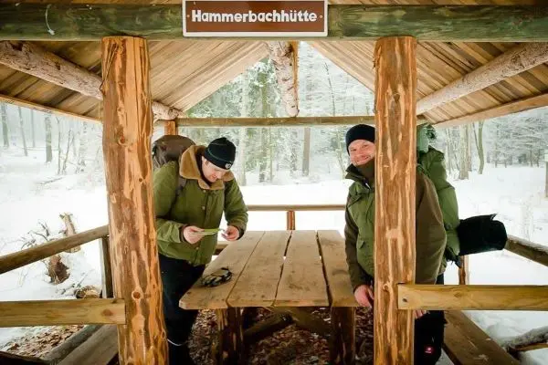 Zwei Personen stehen an einem Tisch in einer Hütte im Schnee