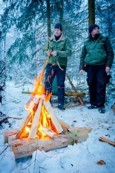 Zwei Personen stehen neben einem Lagerfeuer im Schnee