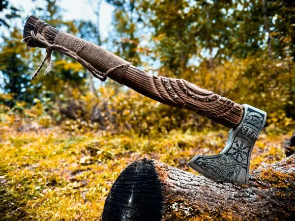 Axt mit kunstvoll geschnitztem Griff auf einem Baumstamm platziert