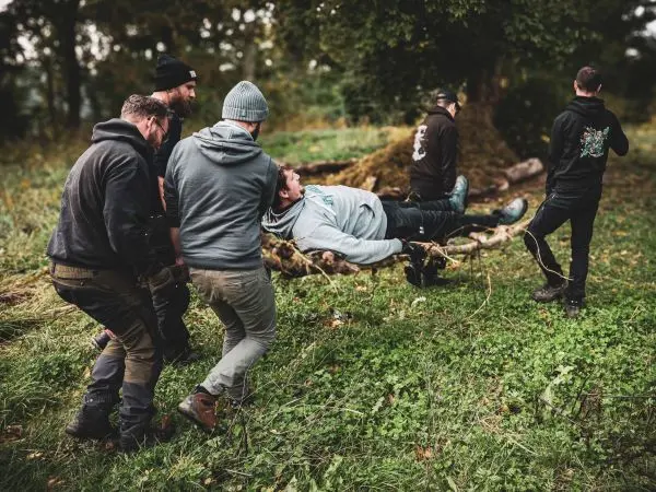 Fünf Personen tragen eine improvisierte Trage mit einer liegenden Person durch das Gras