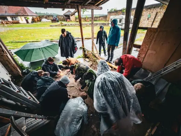 Gruppe arbeitet am Boden, während einige unter Regenschutz stehen und andere Materialien sammeln