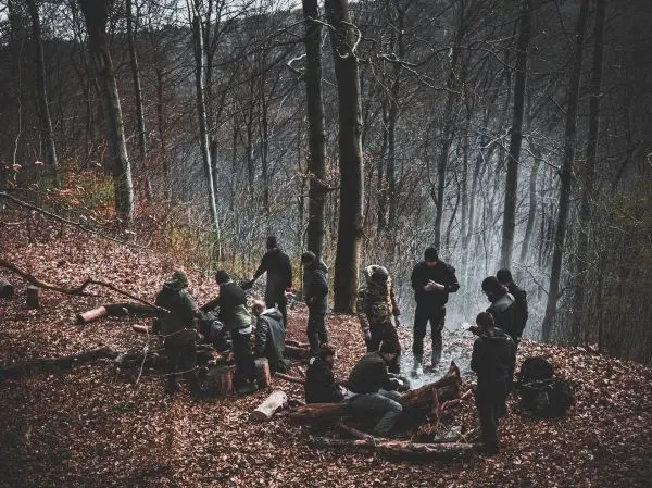 Gruppe arbeitet am Lagerfeuer im Wald, Holzstücke liegen verstreut