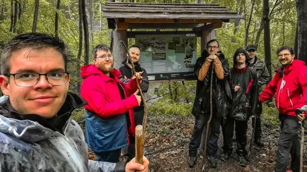 Gruppe hält Wanderstöcke vor einem Informationsschild im Wald