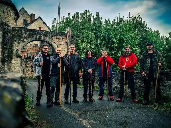 Gruppe mit Wanderstöcken steht auf einem Weg vor einer alten Mauer und Bäumen