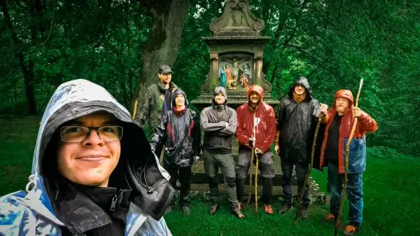 Gruppe von sieben Personen in Regenjacken vor einer Statue im Wald
