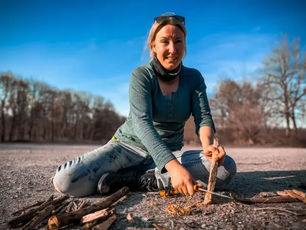 Holzstück wird mit einem Messer bearbeitet, um Zunder vorzubereiten