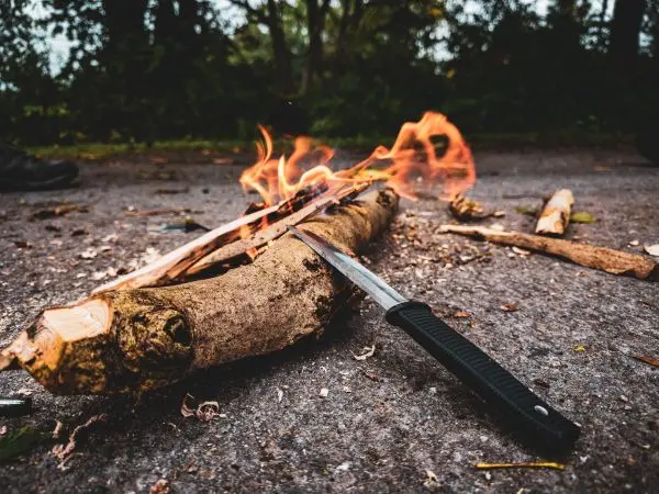 Kleine Flamme brennt auf einem Holzstück neben einem Messer