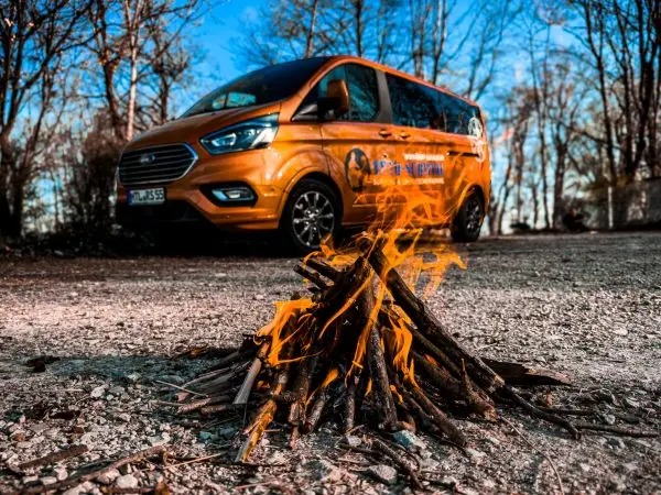 Kleine Flamme brennt auf einem Kiesboden vor einem orangefarbenen Fahrzeug