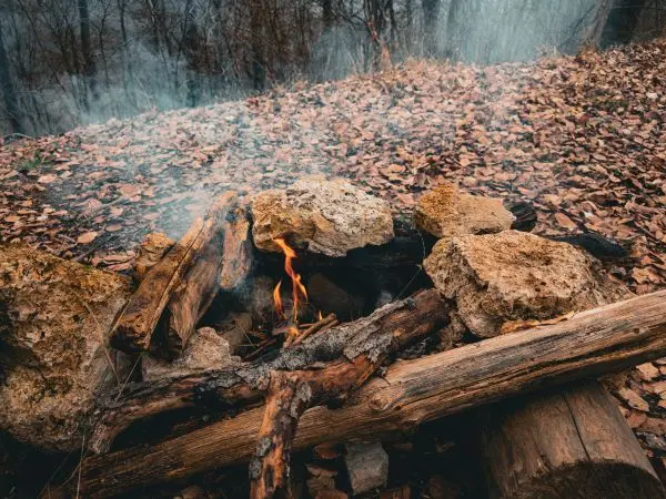 Kleine Flamme zwischen Steinen und Holzscheiten, Rauch steigt auf